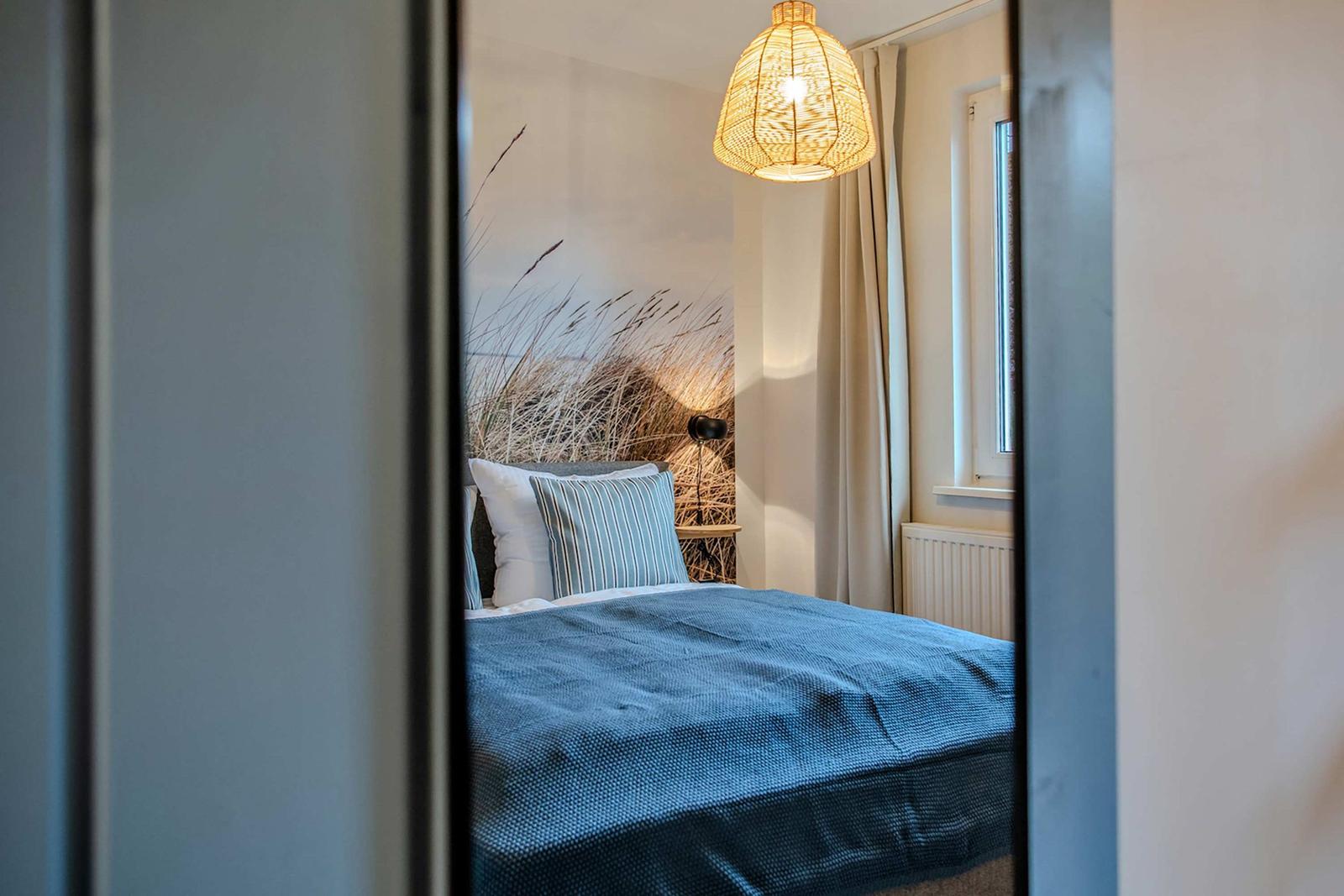 Schlafzimmer mit Bett, Wandbild und Deckenleuchte.