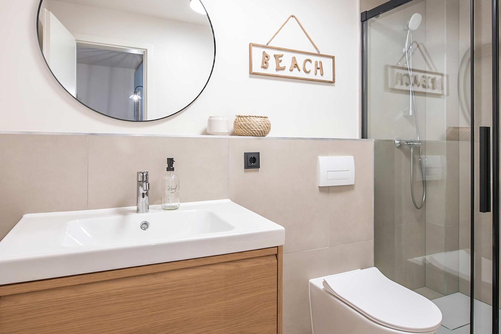 Badezimmer mit Waschbecken, Toilette und Dusche. Wanddekoration mit BEACH.