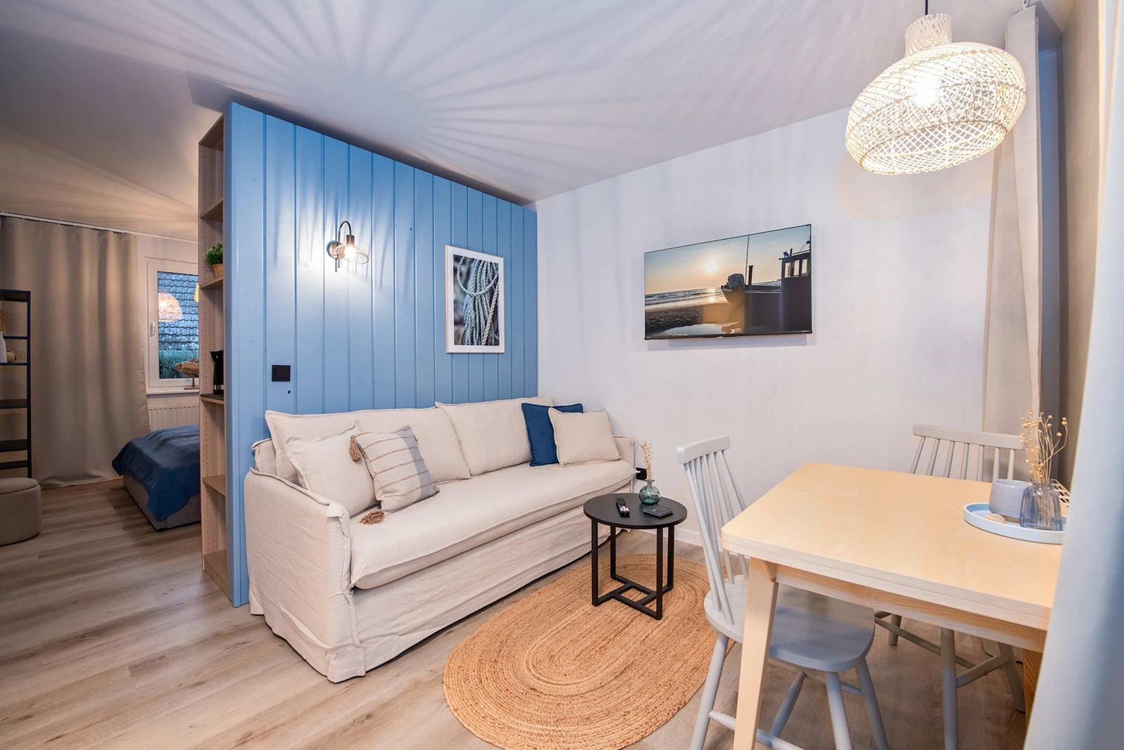 Wohnbereich mit Sofa, Esstisch und blauer Wand. Zimmer im Hintergrund.