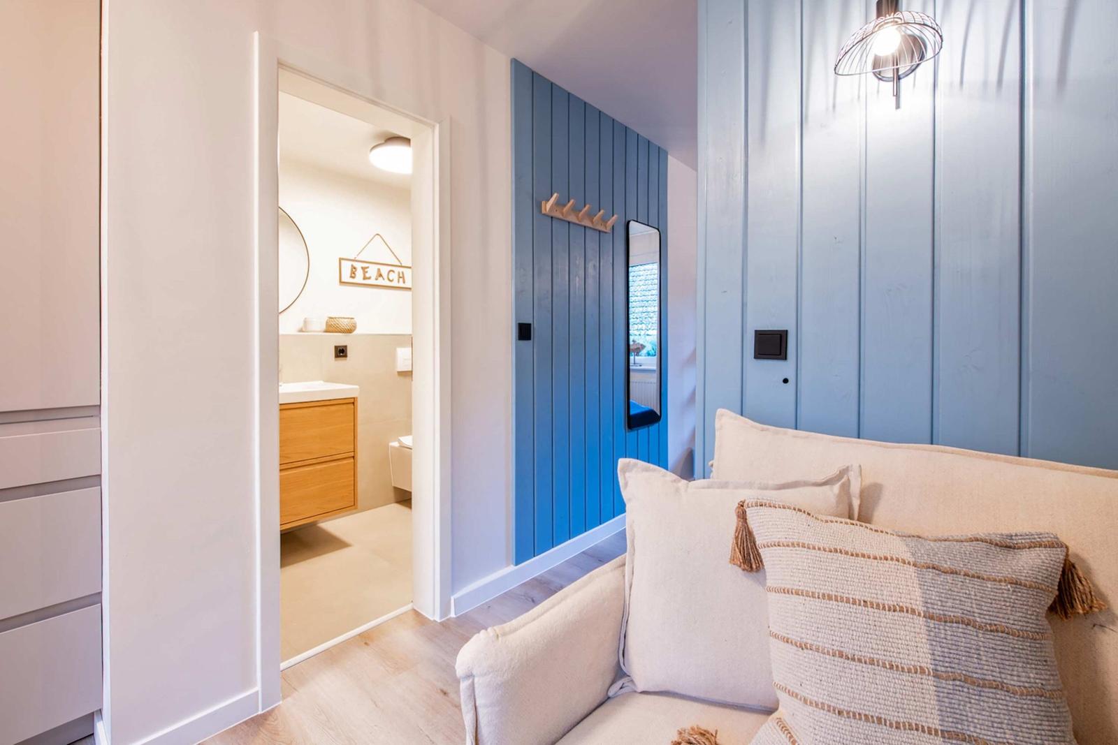 Wohnbereich mit Sofa, blauer Holzwand und Blick in das Badezimmer mit Waschbecken.