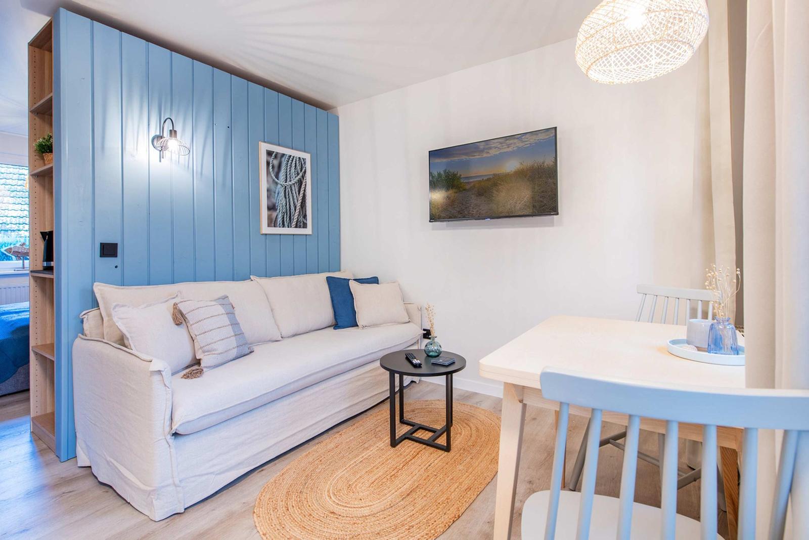 Wohn- und Essbereich mit Sofa, Tisch und Wandbild. Blaue Akzentwand und Holzboden.