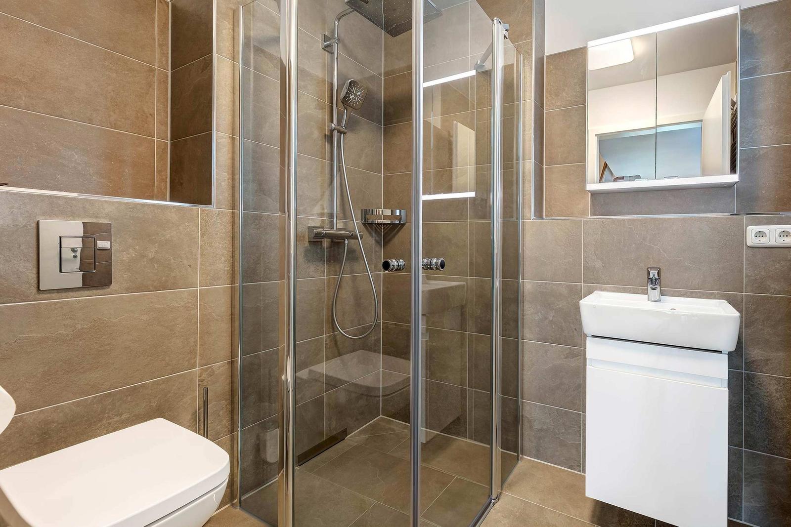 Bad mit Dusche, Waschbecken und Toilette. Fliesenwand und Spiegel.
