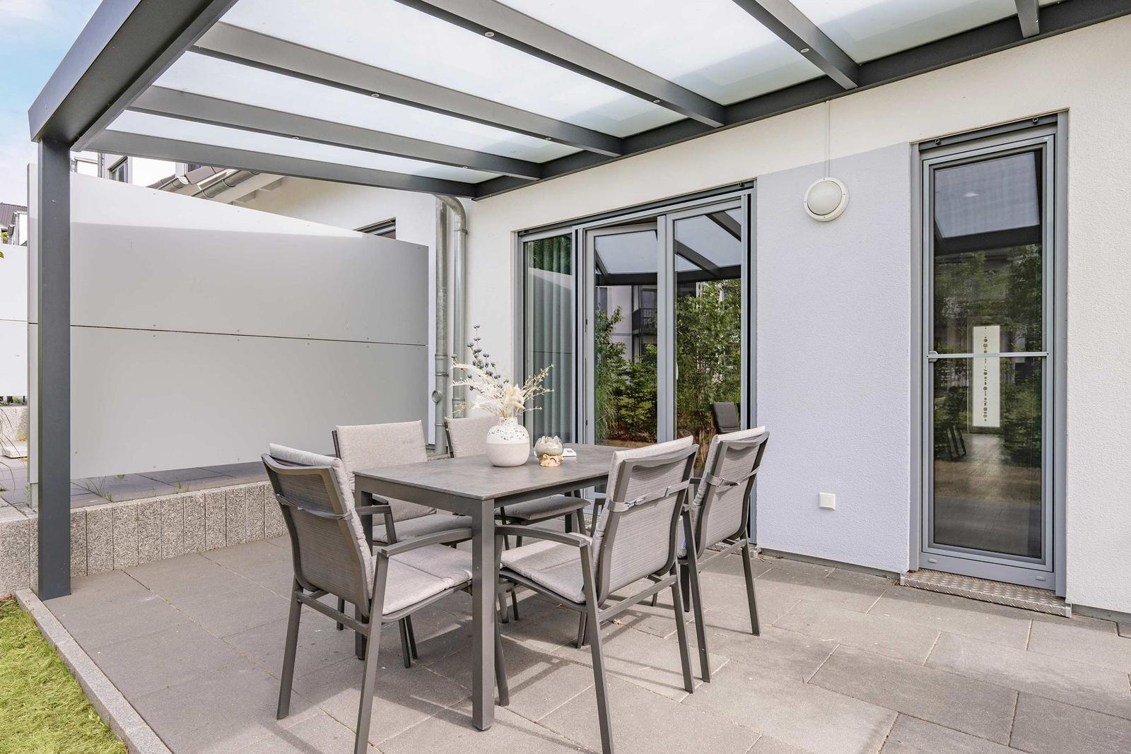 Terrasse mit Sitzgruppe unter Dach, Glasfront und Gartenbereich.