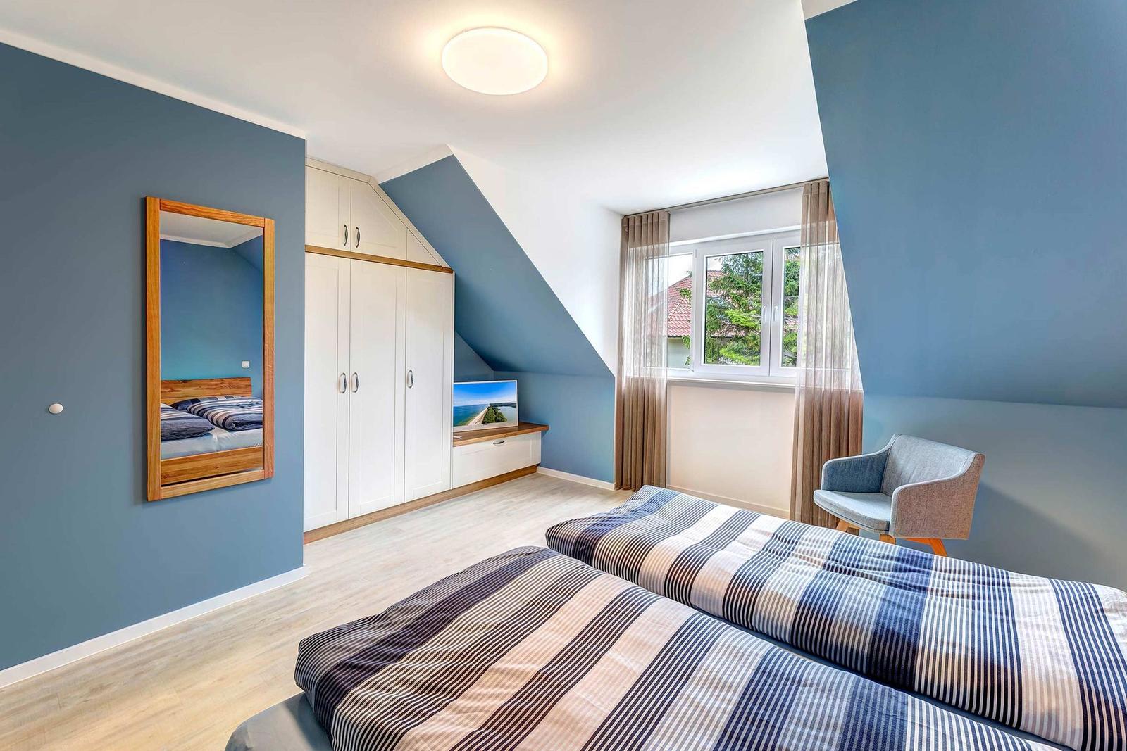 Zimmer mit zwei Betten, Kleiderschrank, Spiegel und Fenster mit Blick auf Außenbereich.