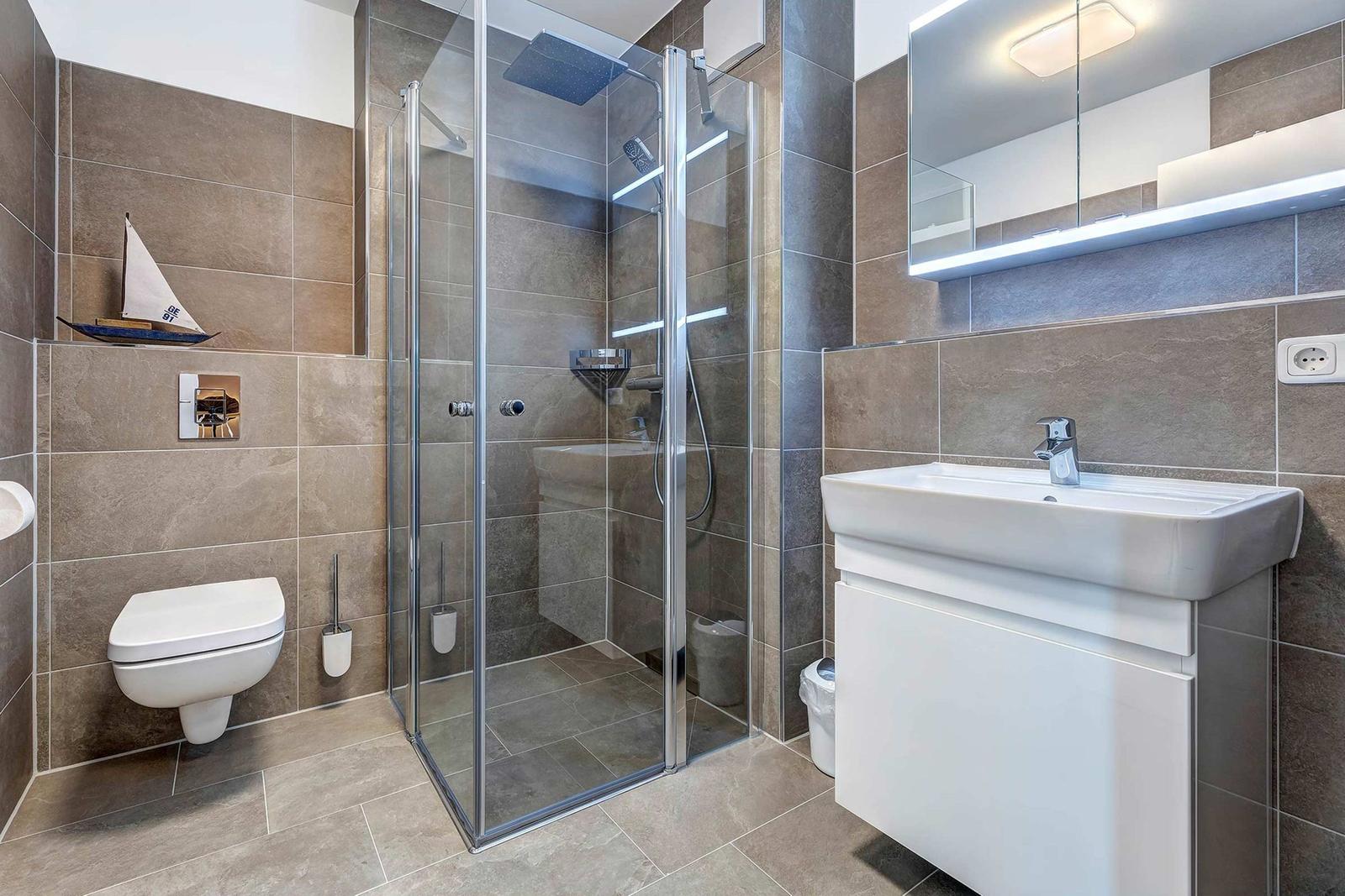 Bad mit Dusche, Waschbecken und Toilette. Wandverkleidung aus Steinoptik.