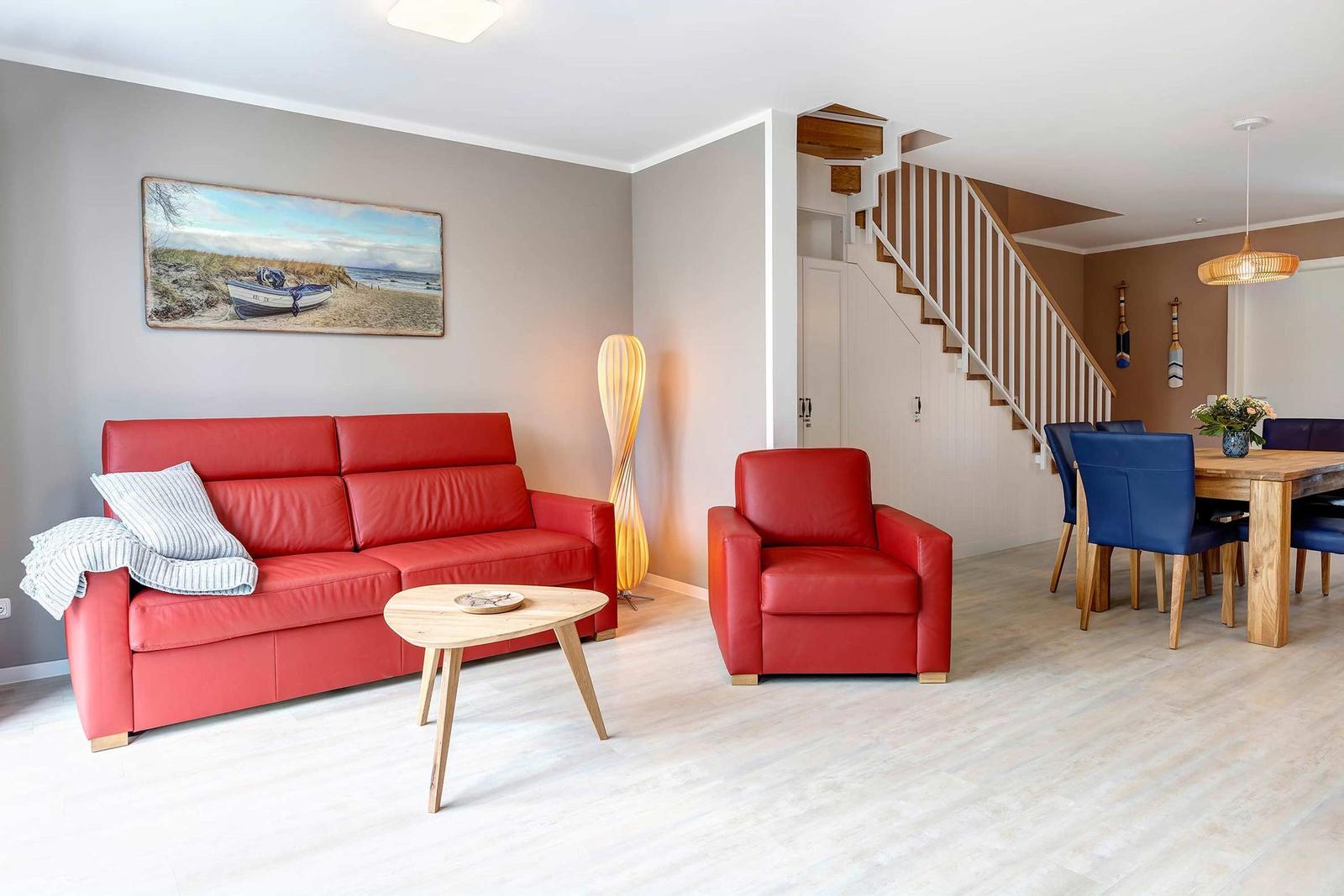 Wohn- und Essbereich mit rotem Sofa, Stuhl und Holztisch. Treppenhaus im Hintergrund.