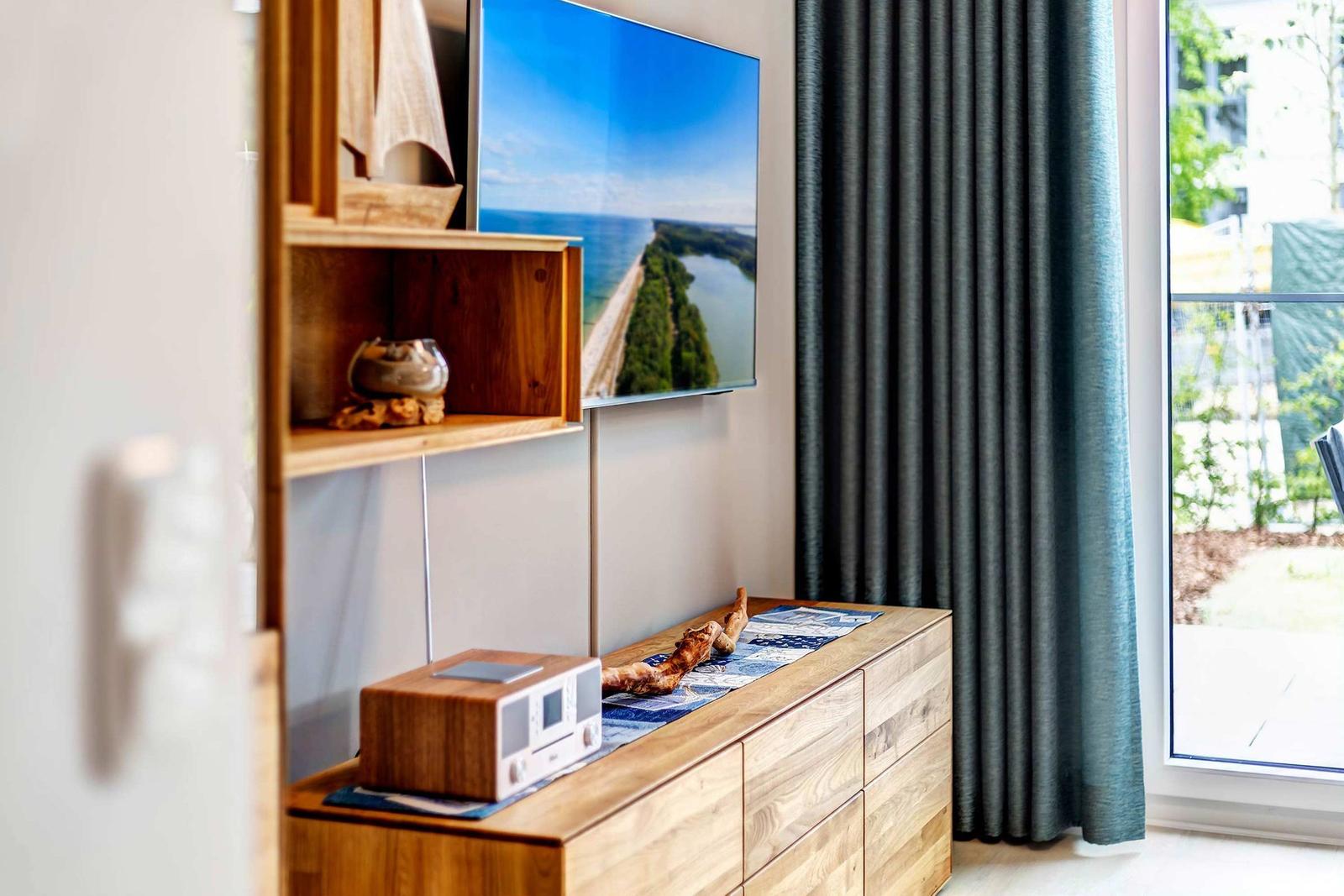 Wohnzimmer mit TV, Holzregal und Fenster mit Vorhang.