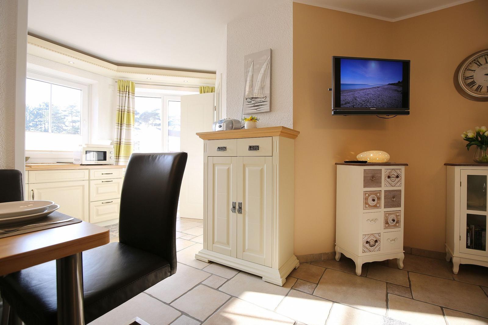 Living and dining area with TV, cabinets, and windows. Tile floor and light interior.