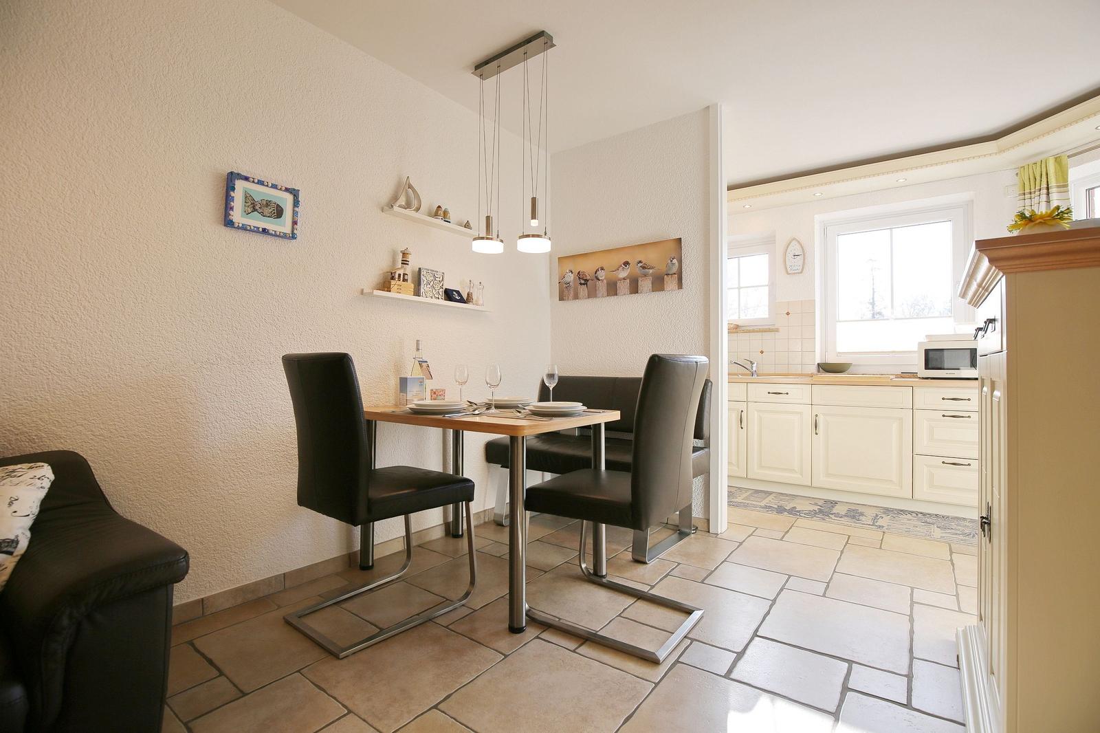 Dining area with table and chairs, kitchen in background, wall decor and lighting.
