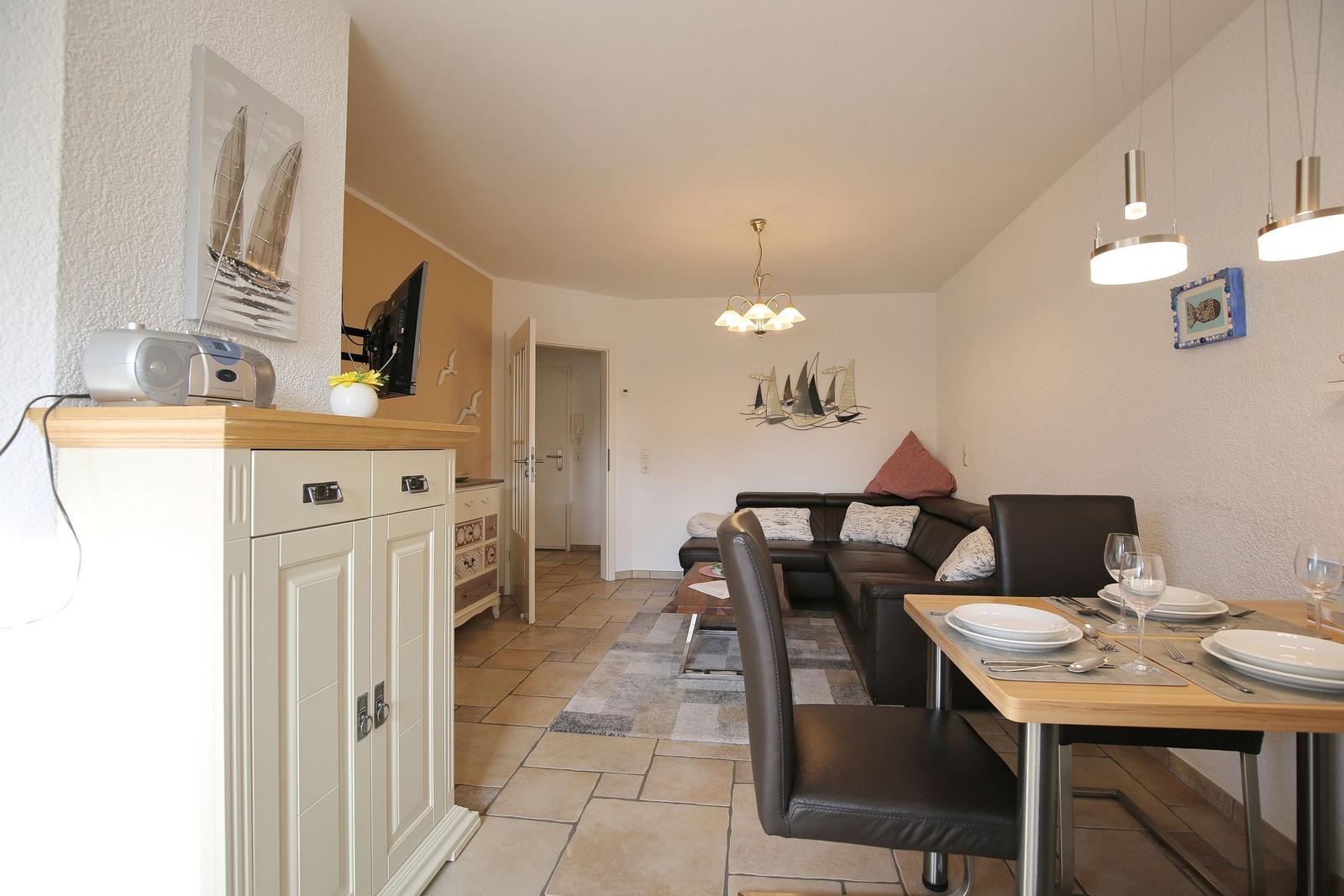 Living and dining area with sofa, table and TV. Wall decoration with sailboats.