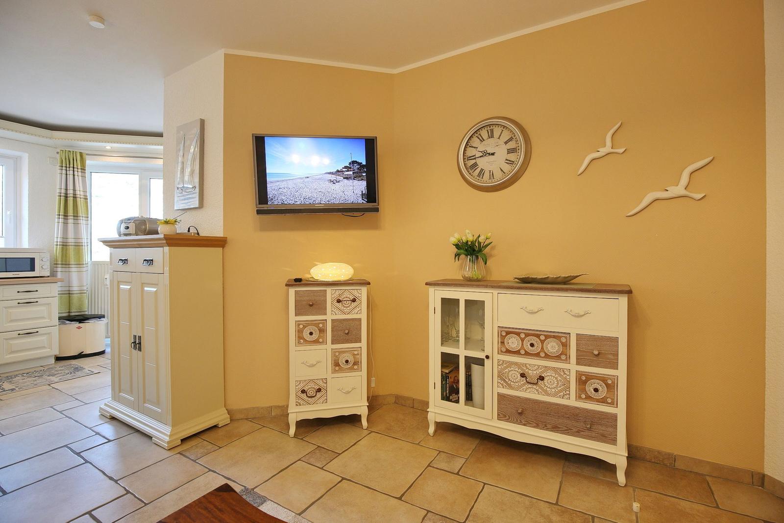 Living area with TV, cabinets, and wall clock. Yellow walls and tiled floor.