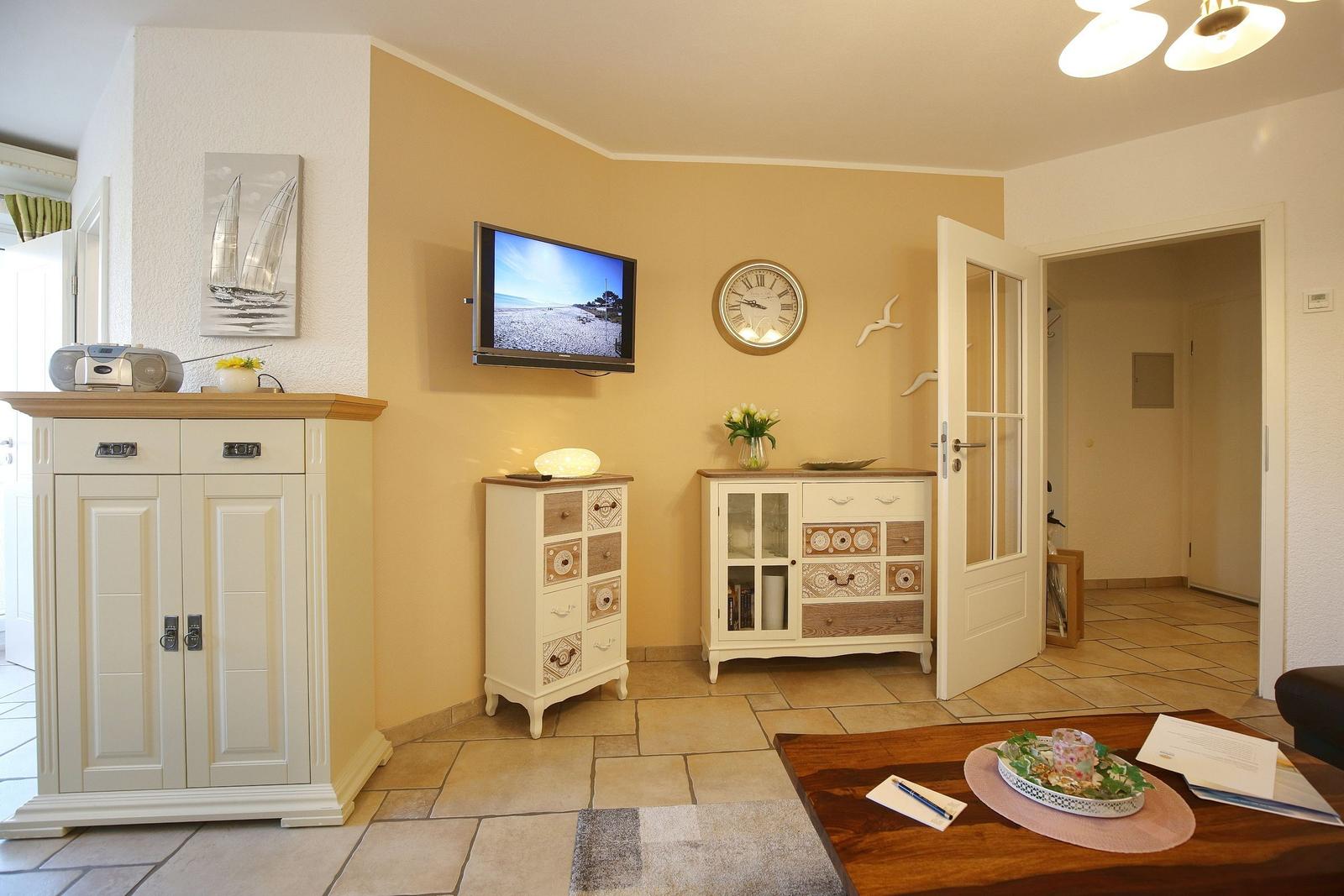 Living room with TV, cabinets, and table. Wall clock and picture on the wall.