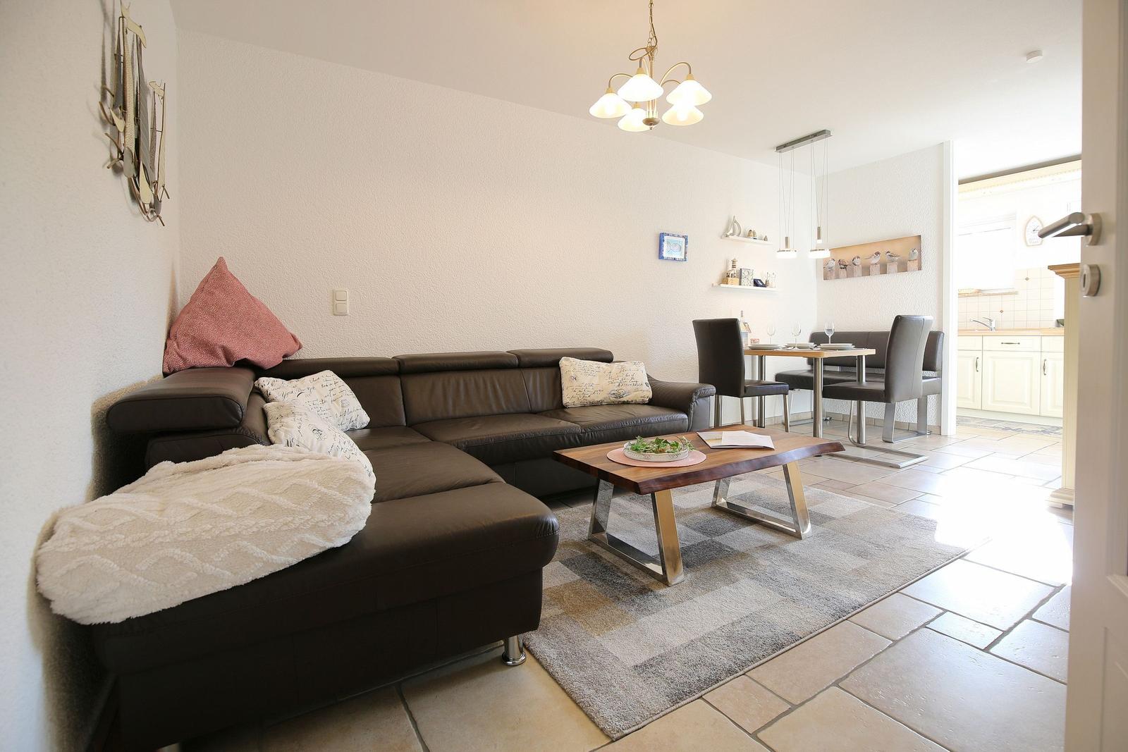 Living and dining area with sofa, table, and kitchen area in the background.