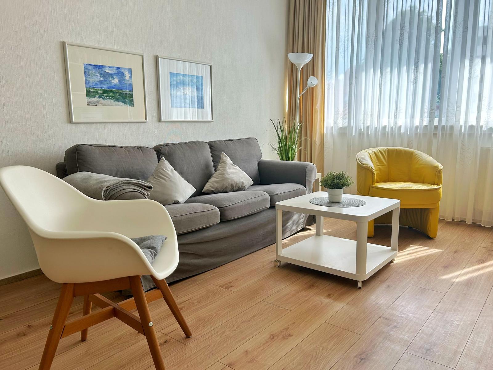 Wohnzimmer mit grauem Sofa, gelber Sessel und weißem Couchtisch.