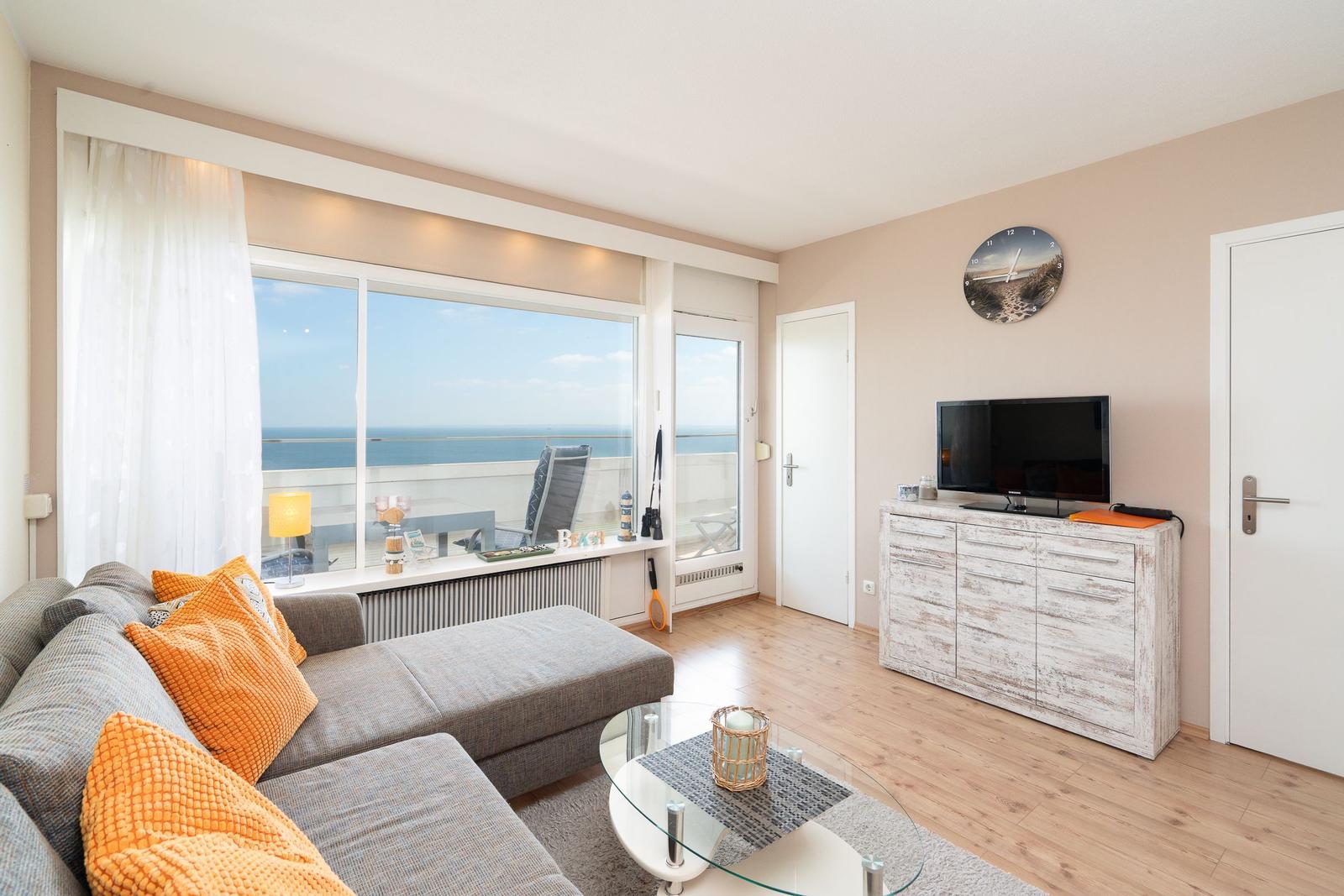 Living room with sofa, TV, and sea view through large windows.