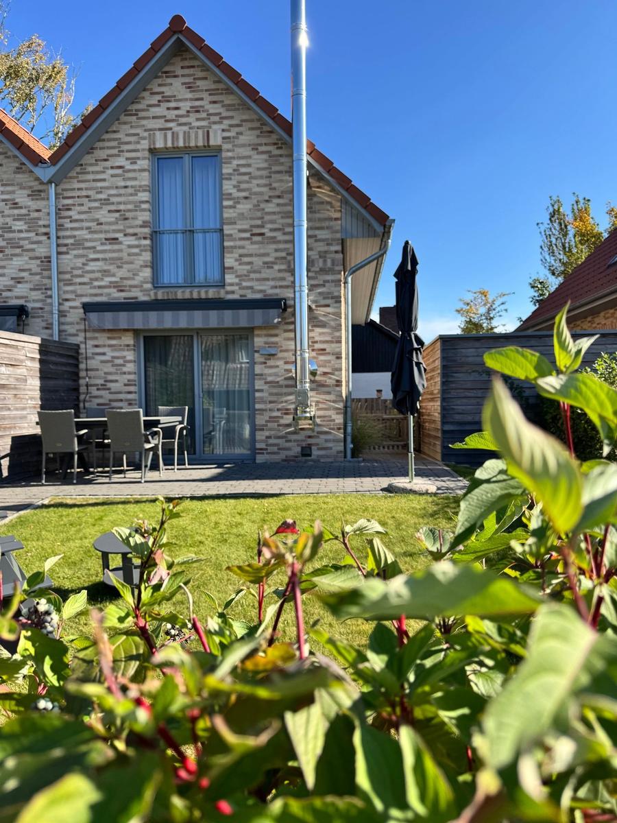 Haus mit Garten, Terrasse und Tisch mit Stühlen. Hintergrund: klarer Himmel.