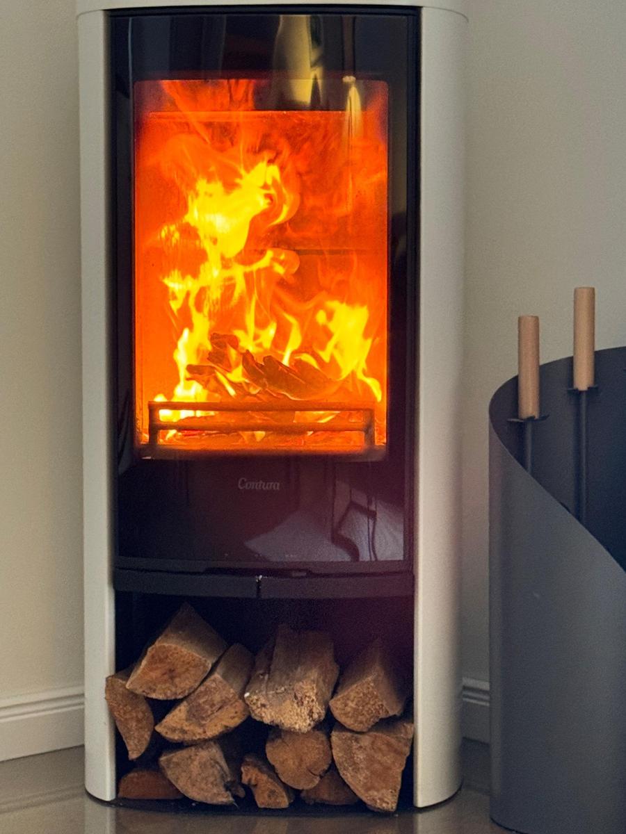Moderne Kaminöfen mit Holzstapel darunter und Feuer im Inneren.