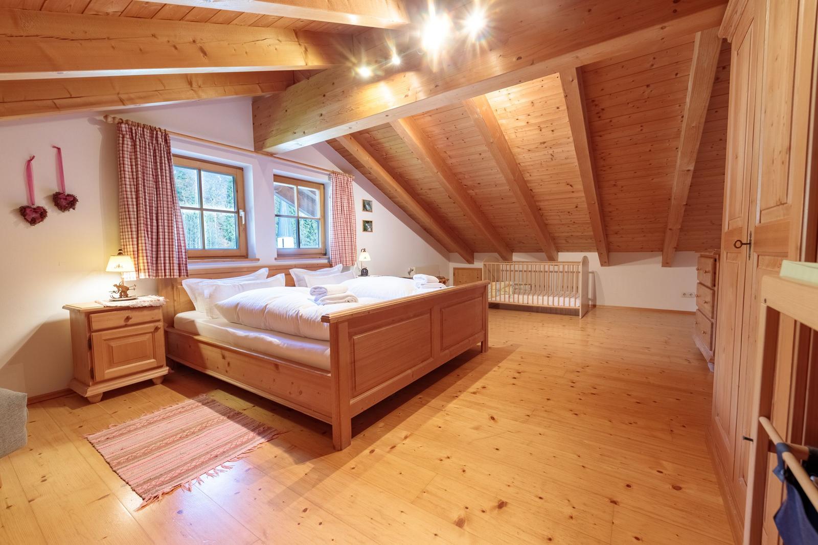 Schlafzimmer mit Holzboden, Dachschräge und Babybett.