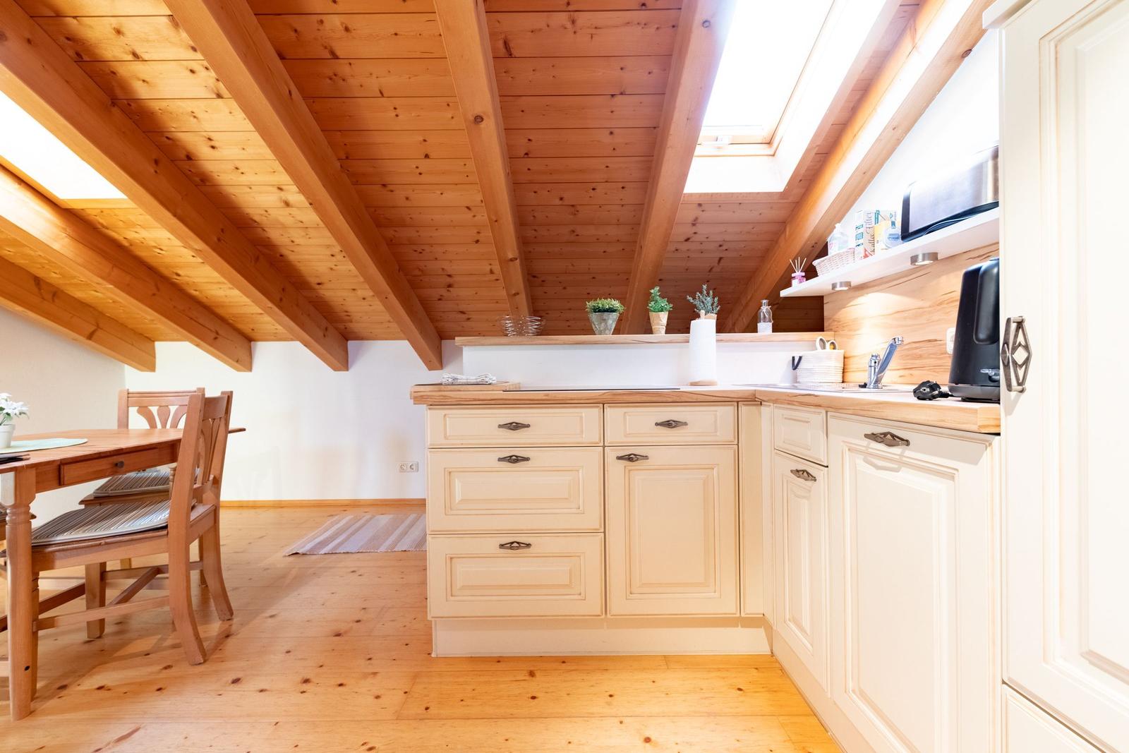 Küche mit Holzdecke und Essbereich. Weiße Schränke und Holzoberflächen.