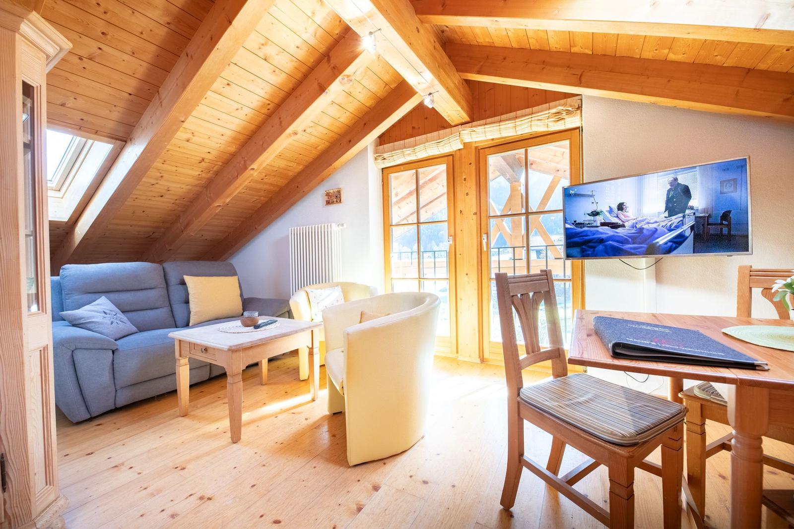 Wohnbereich mit Sofa, Sesseln, Esstisch und TV an der Wand.