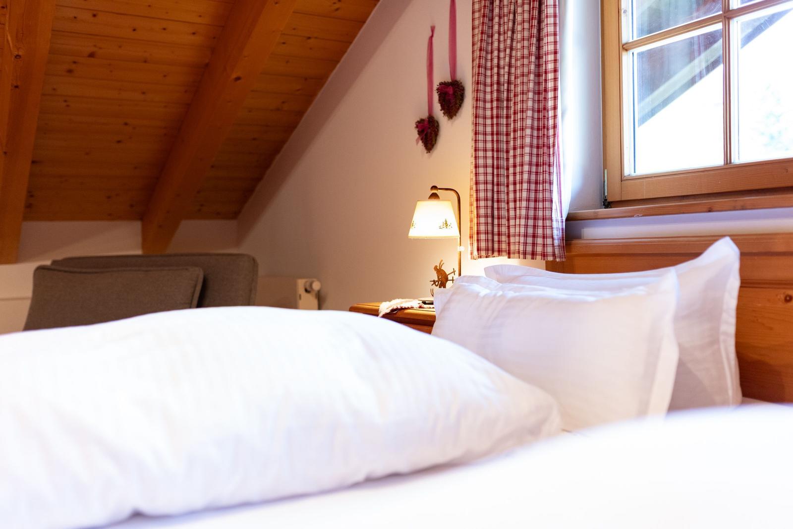 Schlafzimmer mit Bett, Holzdecke und Fenster mit Vorhang.