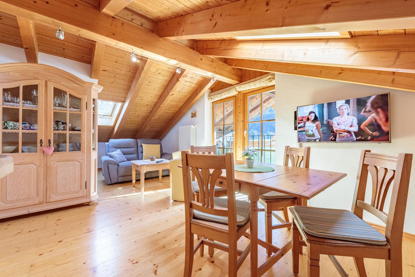Holzgetäfelte Wohnung mit Essbereich, Sofa und TV. Fenster mit Blick auf die Berge.