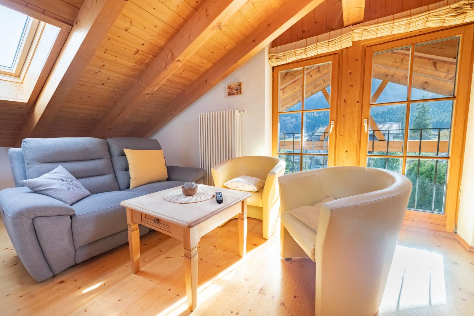 Wohnzimmer mit Sofa, zwei Sesseln und Tisch unter Holzdecke mit Blick auf Berge.