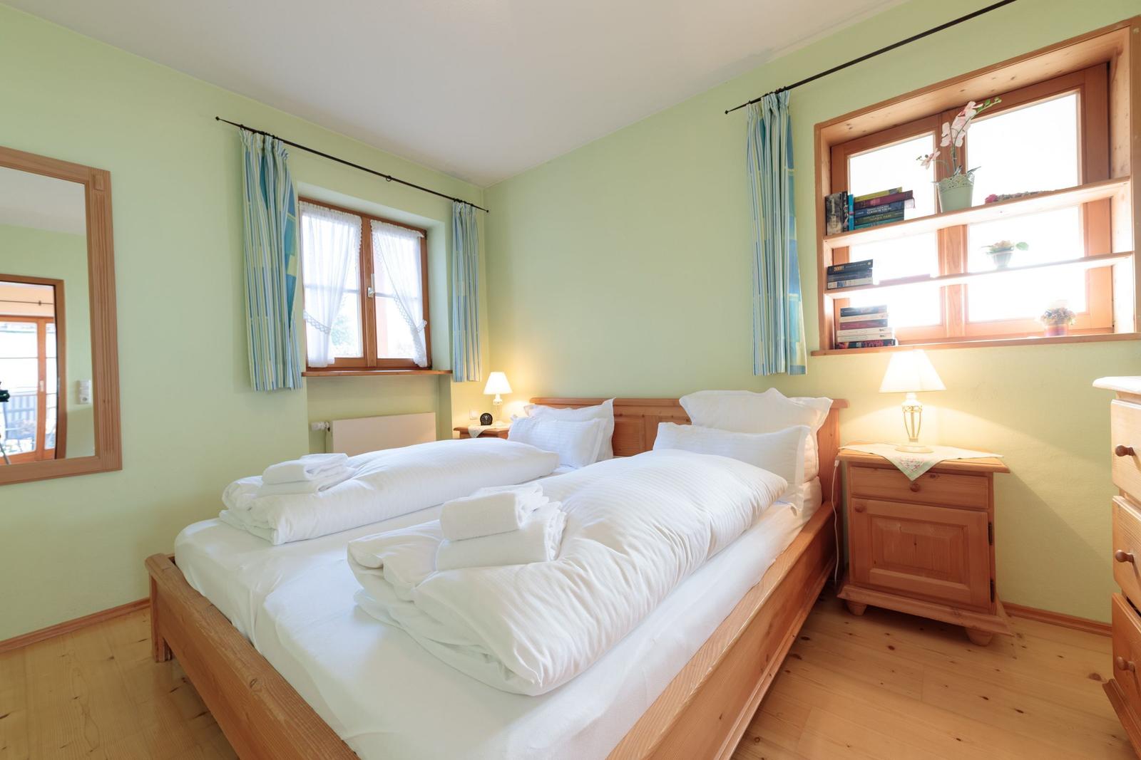 Schlafzimmer mit Holzbett, Fenstern und Nachttischen.