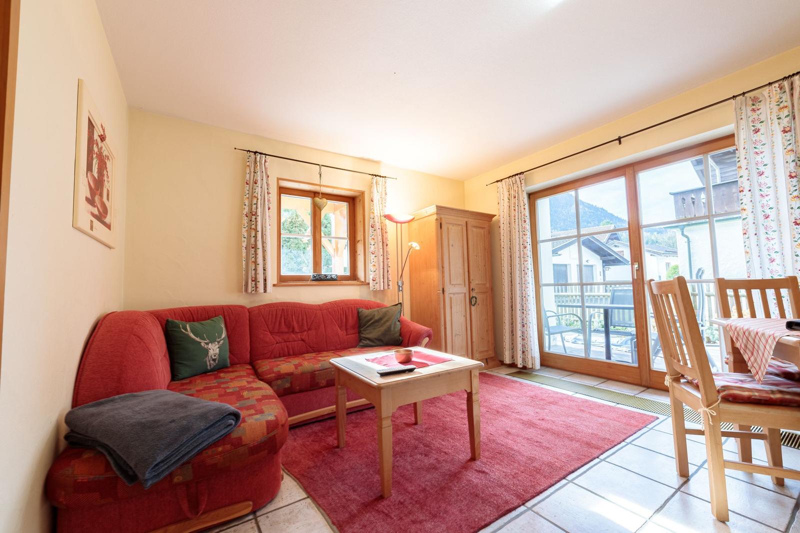 Ein Wohnzimmer mit rotem Sofa, Holztisch und Blick auf Balkon.