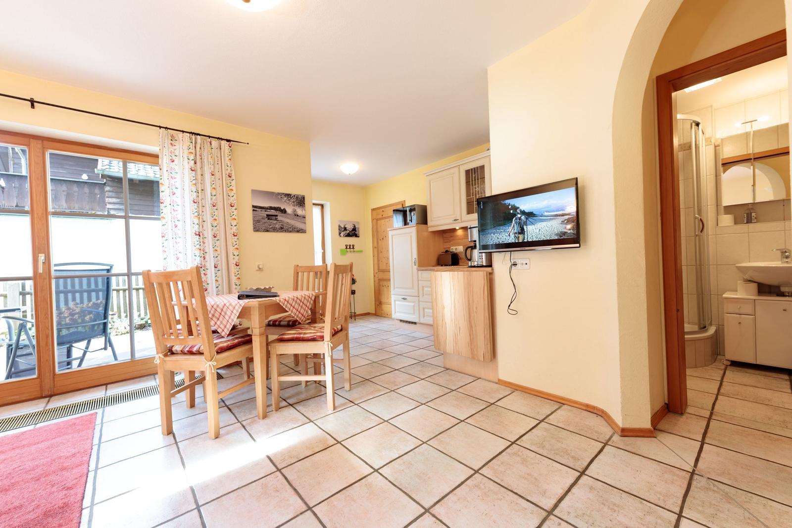 Wohnküche mit Essbereich, TV und Bad. Terrasse mit Gartenblick.