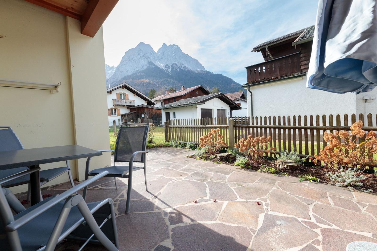 Terrasse mit Tisch und Stühlen, Blick auf Berge und umliegende Häuser.