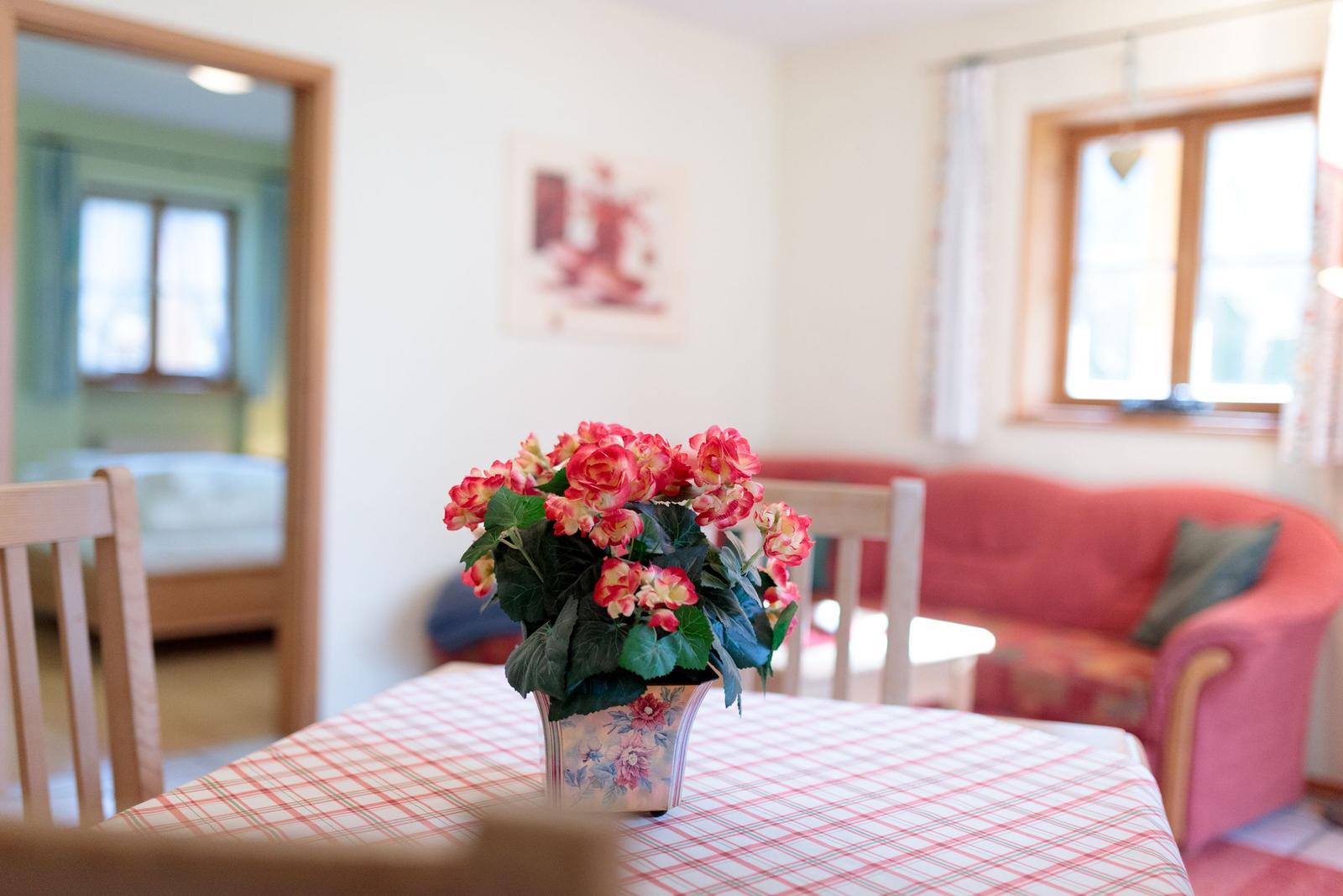 Tisch mit Blumen, rote Couch und Fenster im Hintergrund.