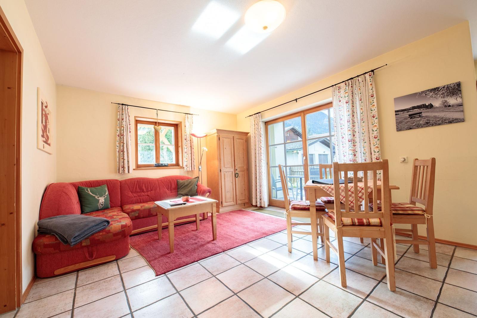 Wohn- und Essbereich mit rotem Sofa, Holztisch und Stühlen, Fenster und Tür zur Terrasse.