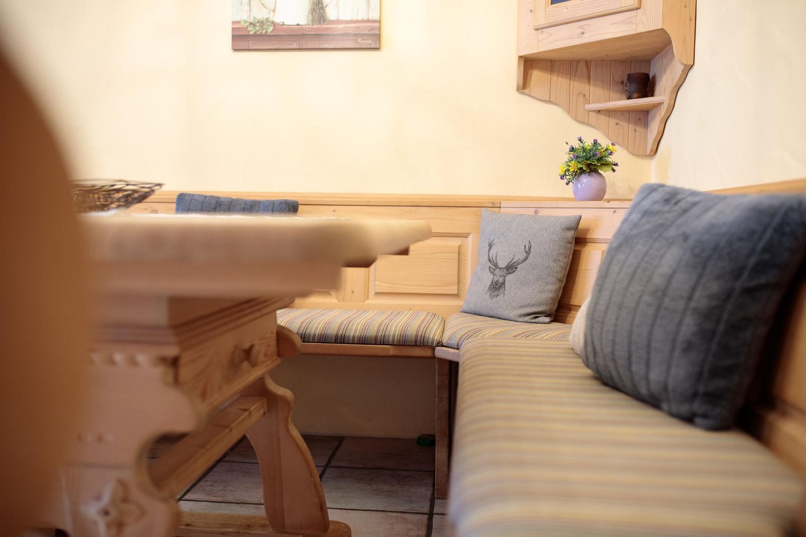 Holzbank mit Kissen und Blumenarrangement an der Wand