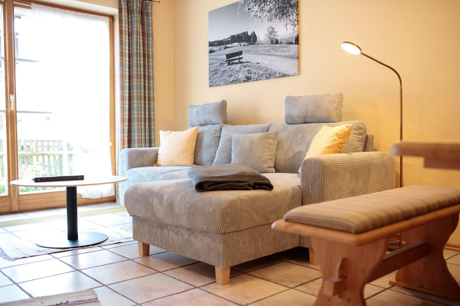 Ein Wohnzimmer mit Sofa, Beistelltisch und Bodenfliesen. An der Wand hängt ein Bild.
