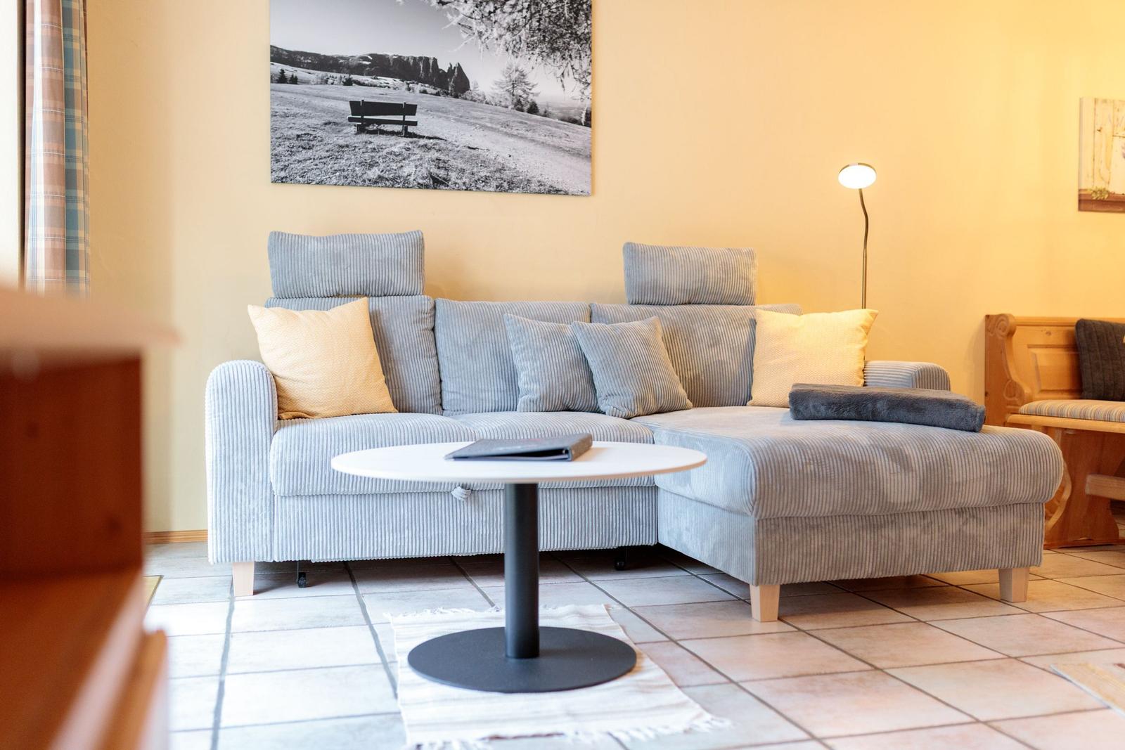 Ein Wohnzimmer mit grauem Sofa, runden Tisch und Wandbild.