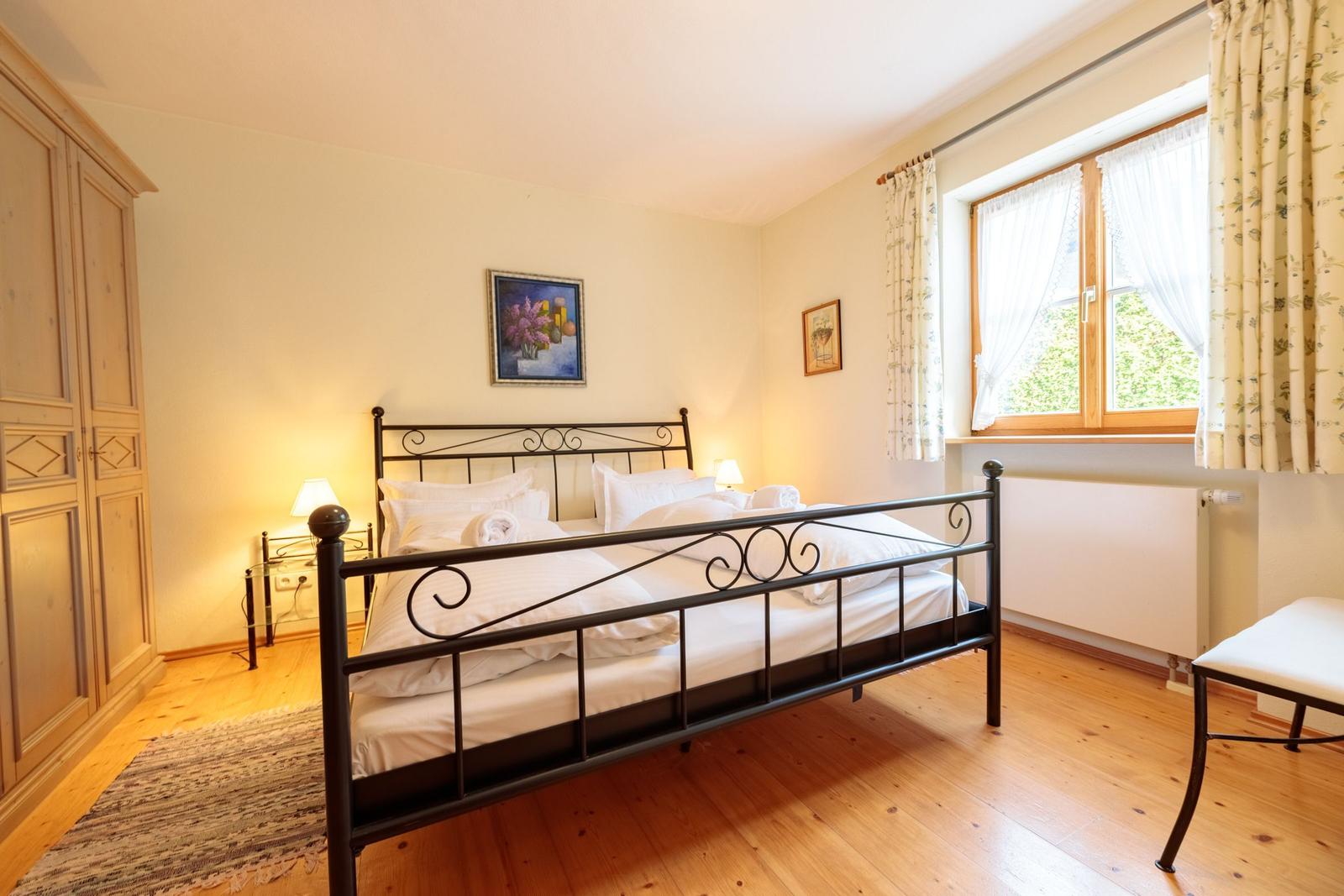 Schlafzimmer mit Doppelbett, Holzboden und Fenster mit Vorhängen.