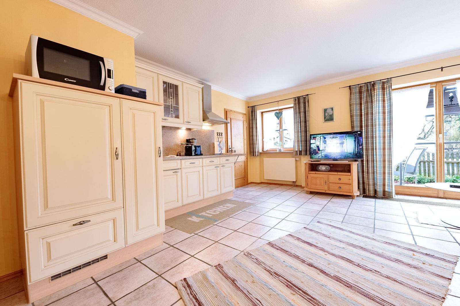 Küche mit Mikrowelle und Wohnzimmer mit TV und Terrassentür.
