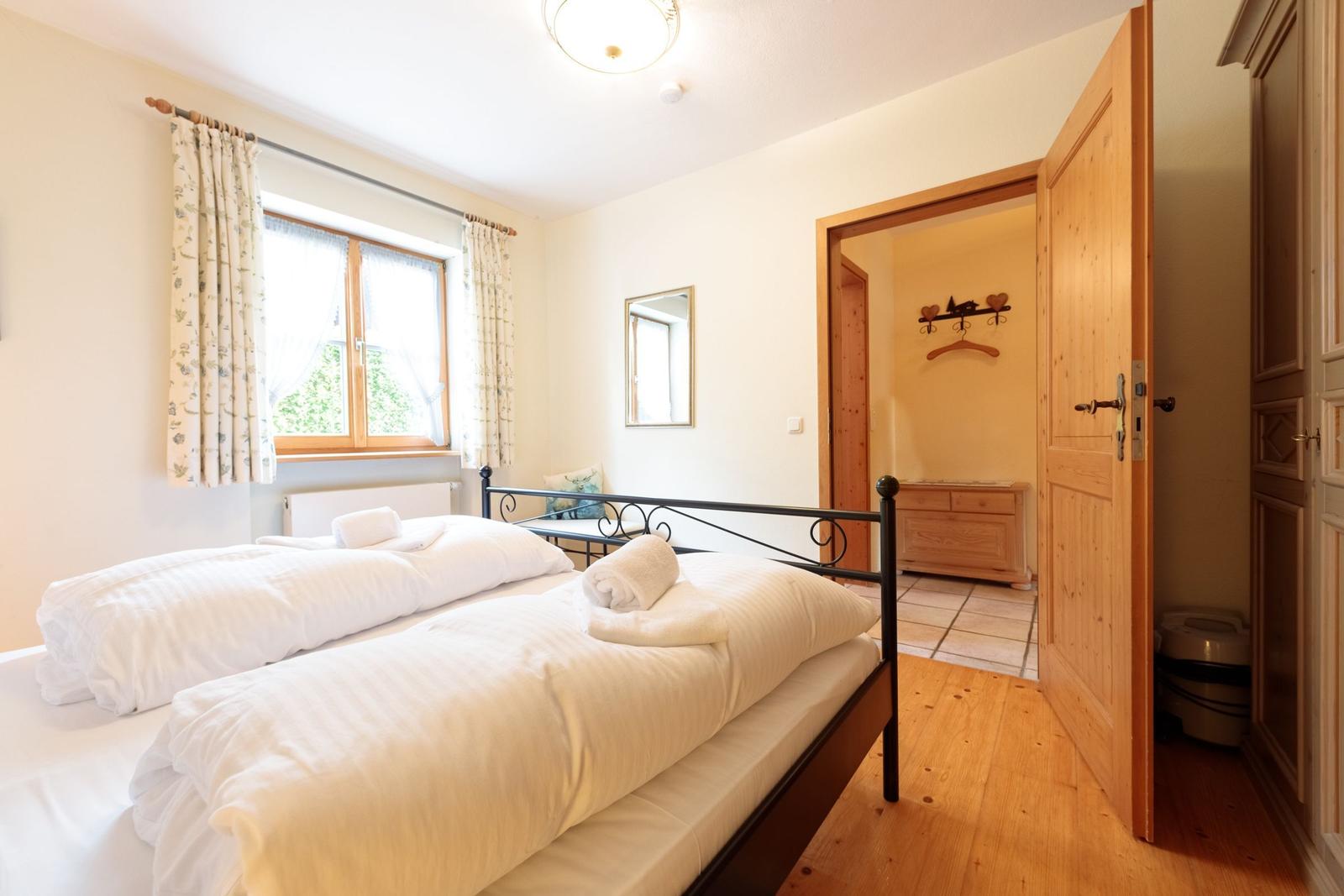 Schlafzimmer mit Doppelbett, Fenster und Holzboden. Tür führt in einen Ankleidebereich.