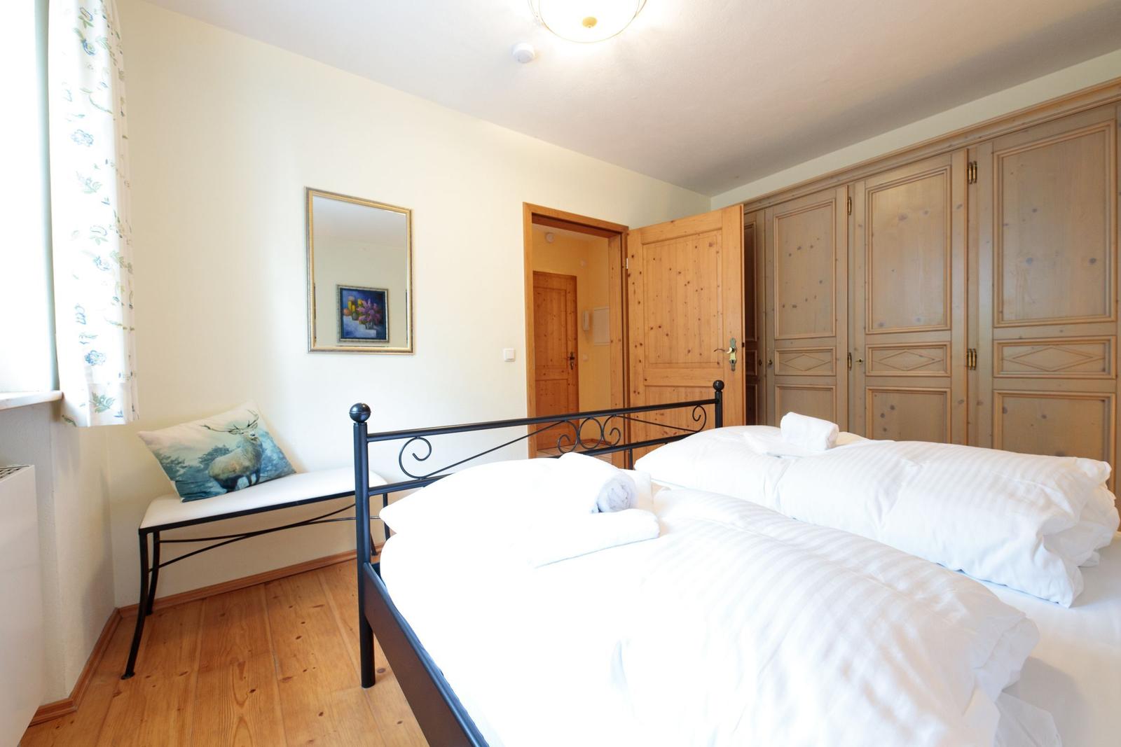 Schlafzimmer mit Doppelbett, Holzmöbel und Fensterbank mit Kissen.