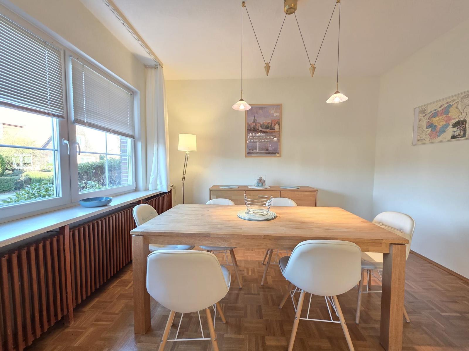 Esszimmer mit Holztisch, weißen Stühlen und Fenster mit Jalousien.