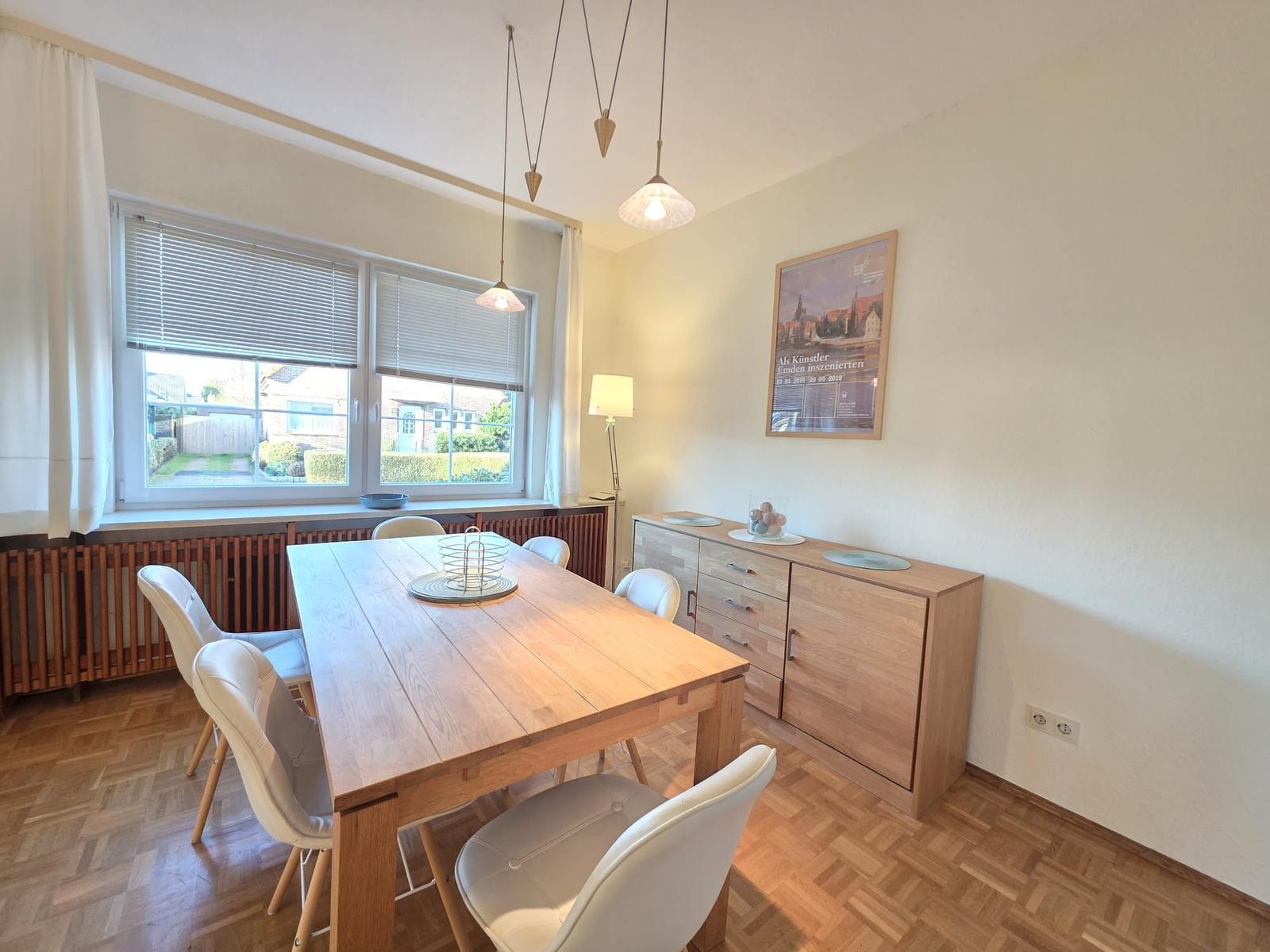 Esszimmer mit Holztisch, weißen Stühlen und Fensterblick auf Garten.