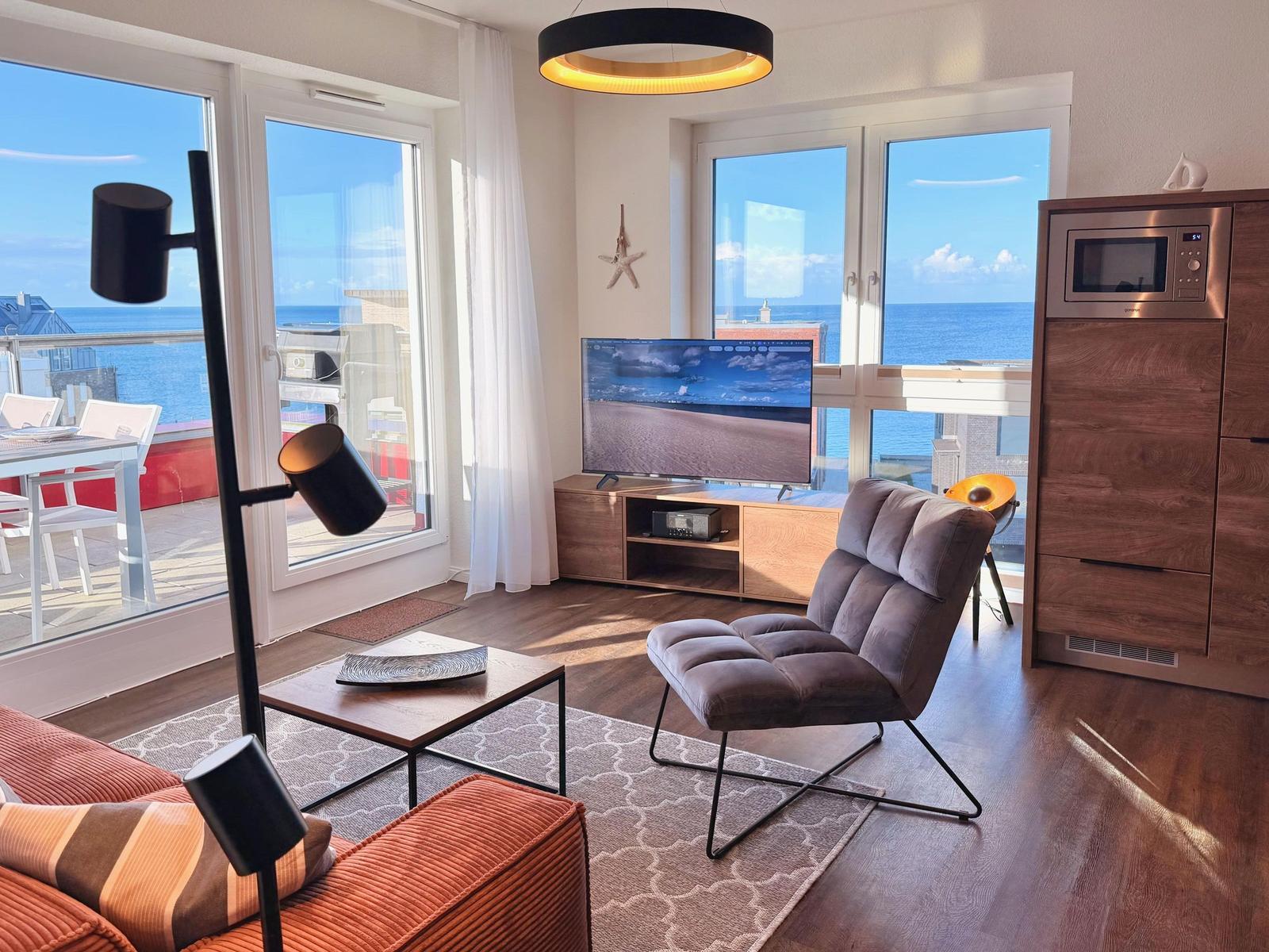 Wohnzimmer mit Meerblick, Sofa, Sessel und Fernseher.