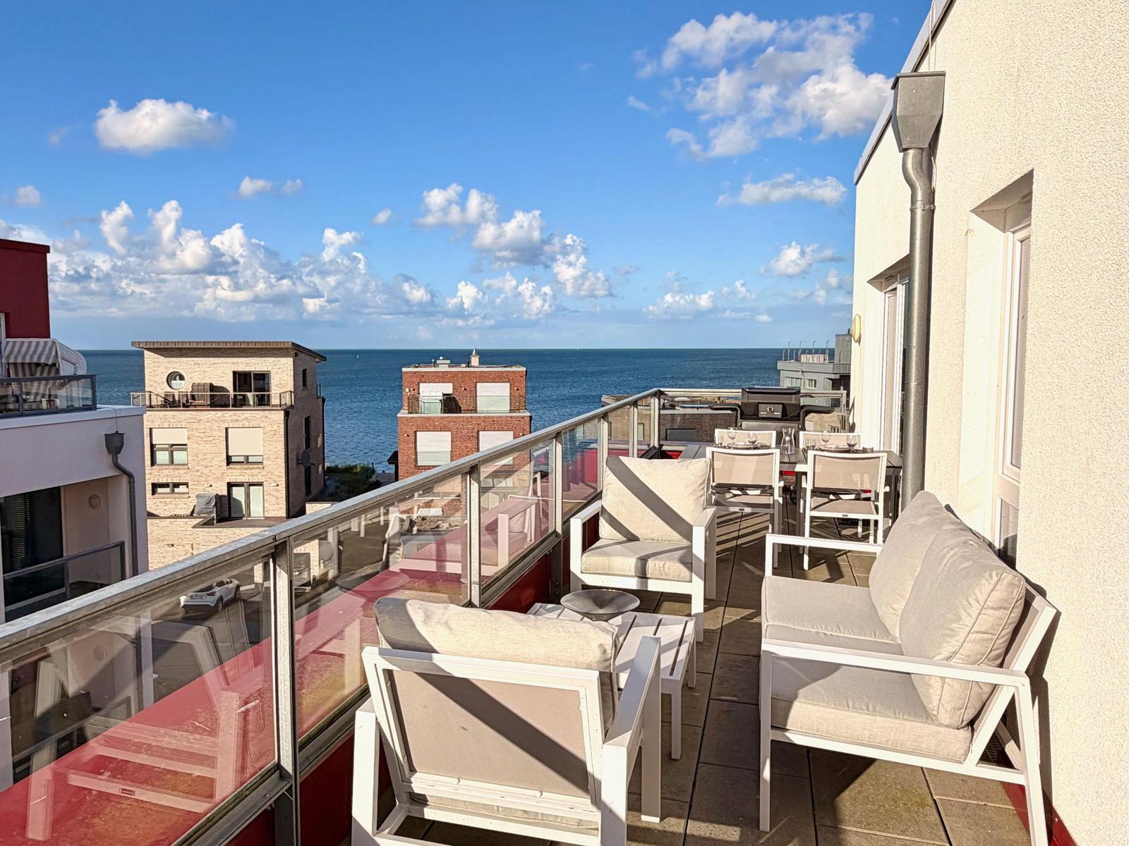 Terrasse mit Sitzgelegenheiten und Meerblick. Glasgeländer und moderne Möbel.