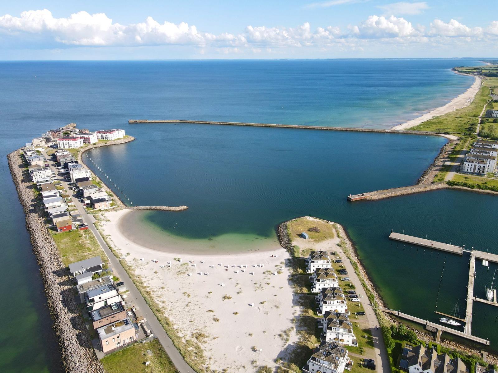 Aerielansicht eines Hafens mit Strand, Bootshäfen und Wohnhäusern an der Küste.
