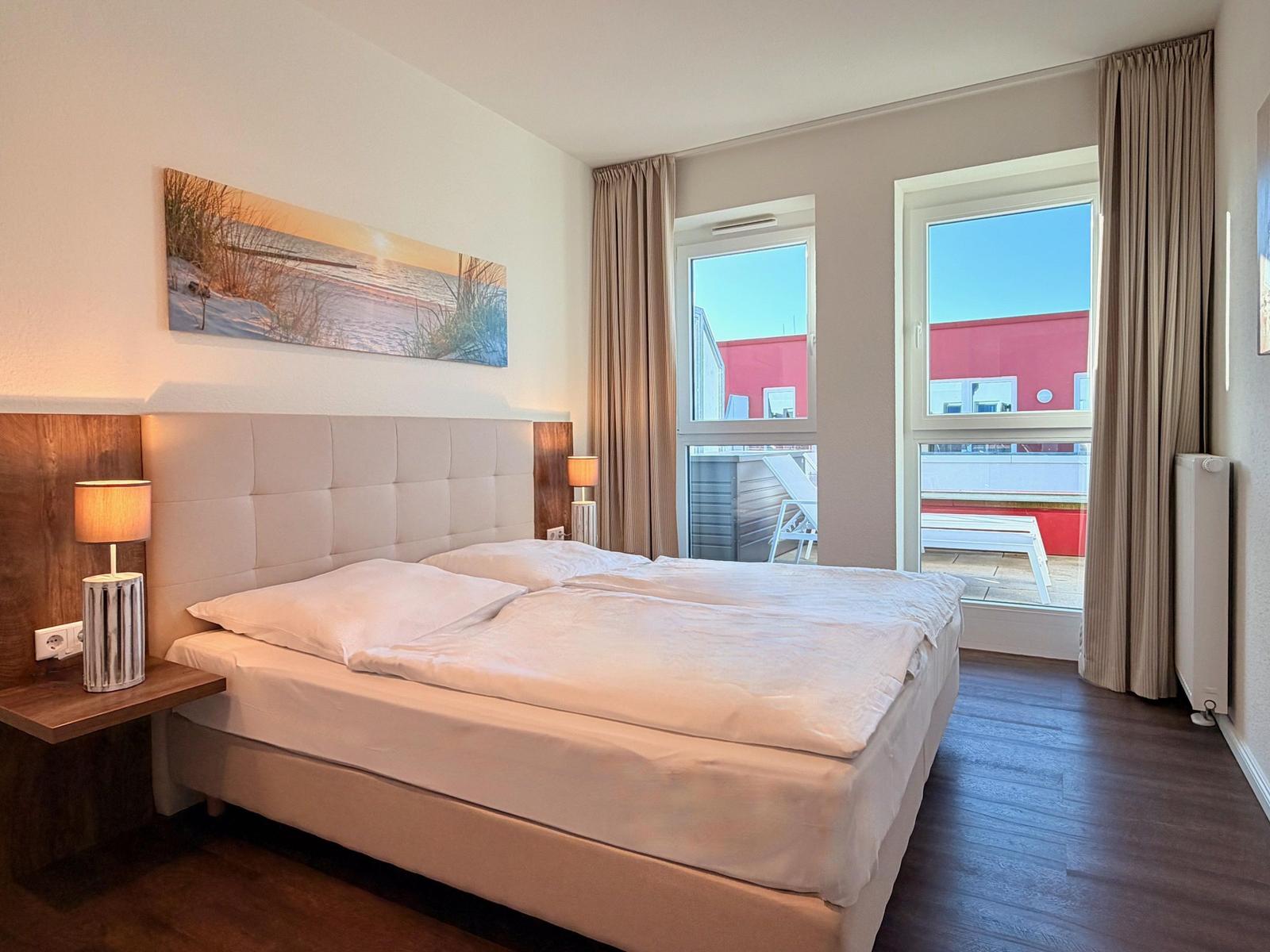 Schlafzimmer mit Doppelbett, Fenster und Balkonblick.
