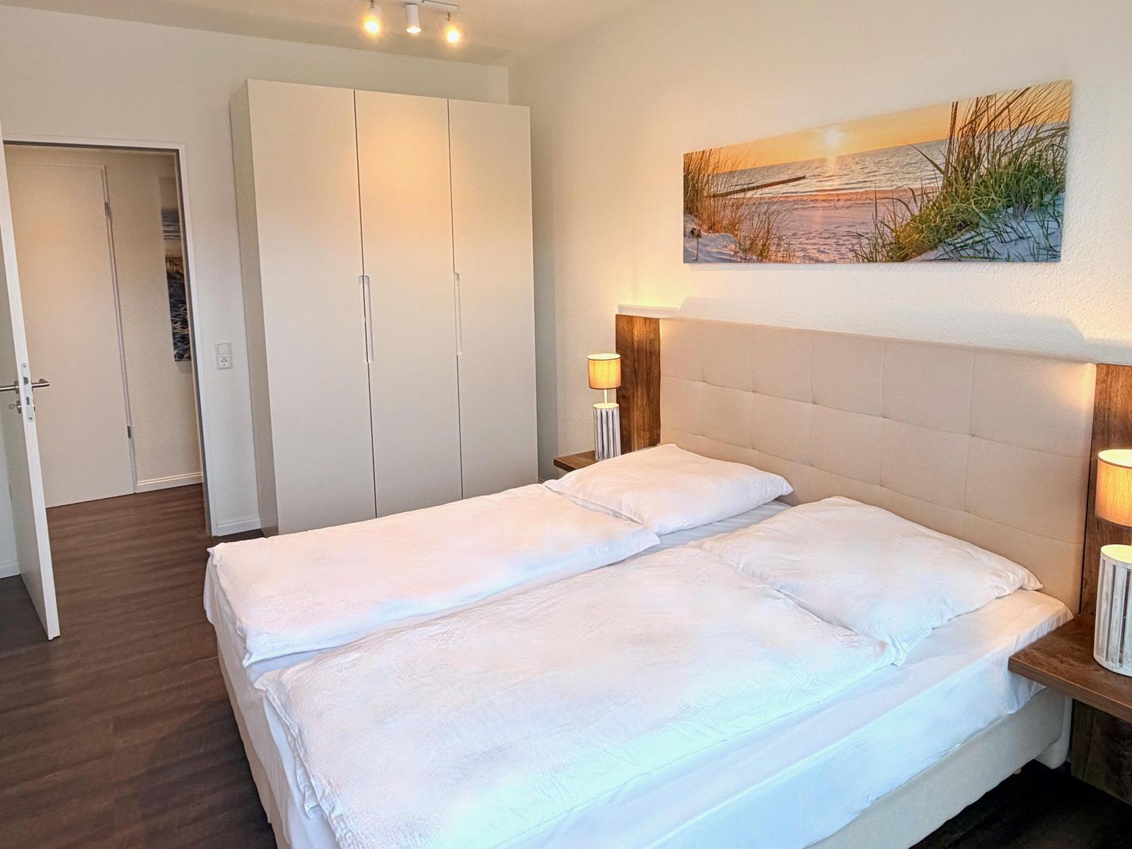 Schlafzimmer mit Doppelbett, Kleiderschrank und Wandbild.