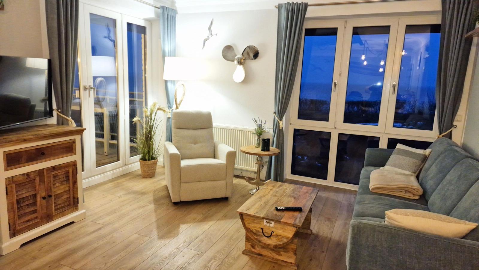 Wohnzimmer mit Sofa, Sessel, Fernseher und großen Fenstern mit Blick.