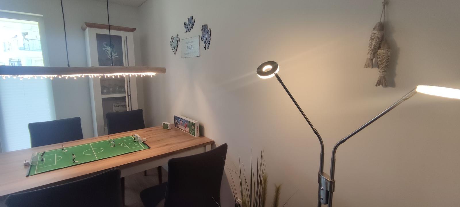 Dining area with table, chairs, and football table. Wall lighting and floor lamp.