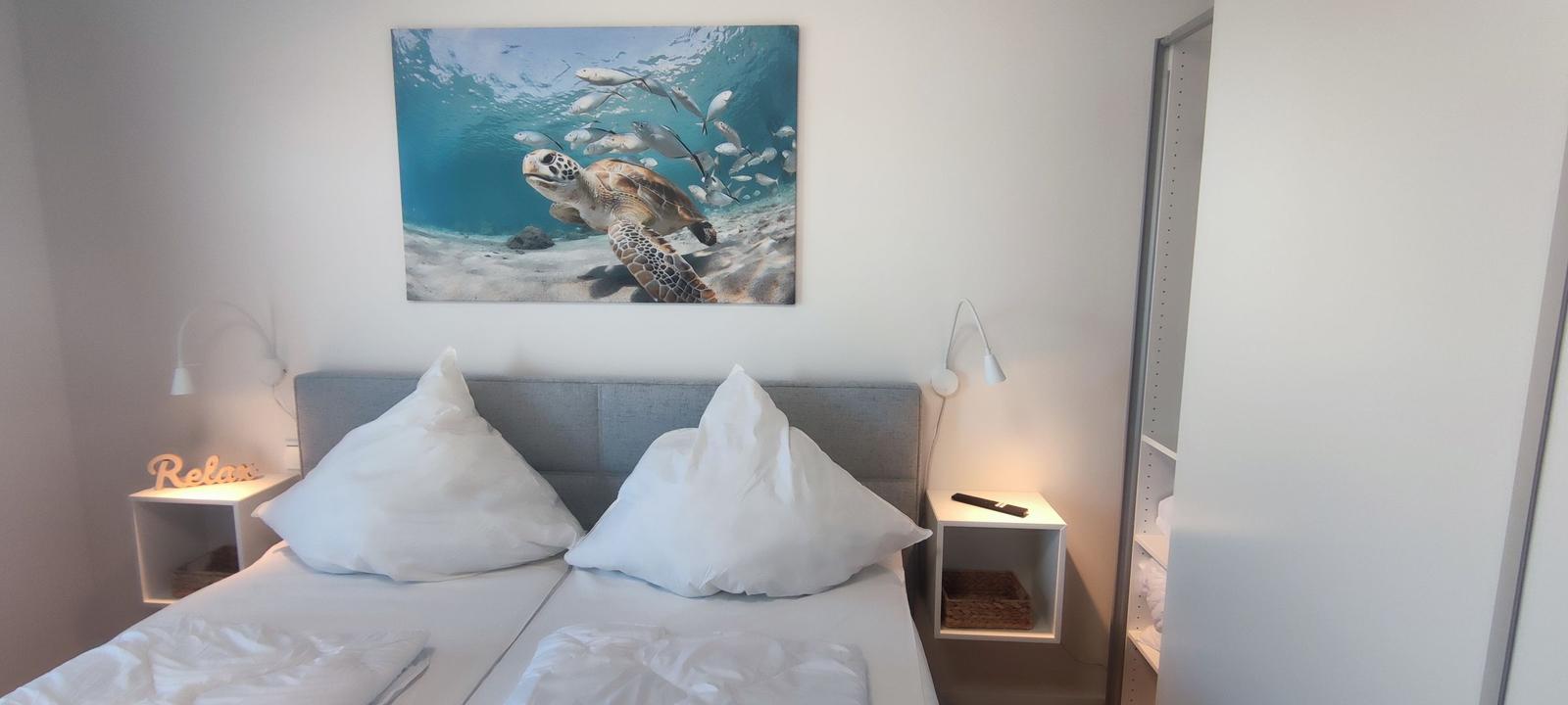Bedroom with double bed, wall art of a turtle, and two bedside tables.